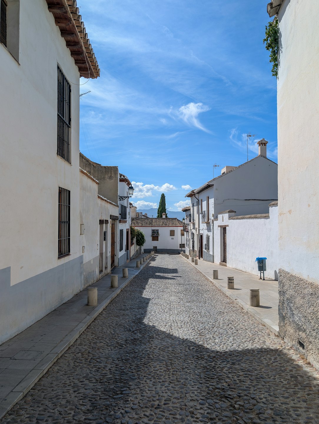 Empty cobblestone street lined with white buildings in a historic town.