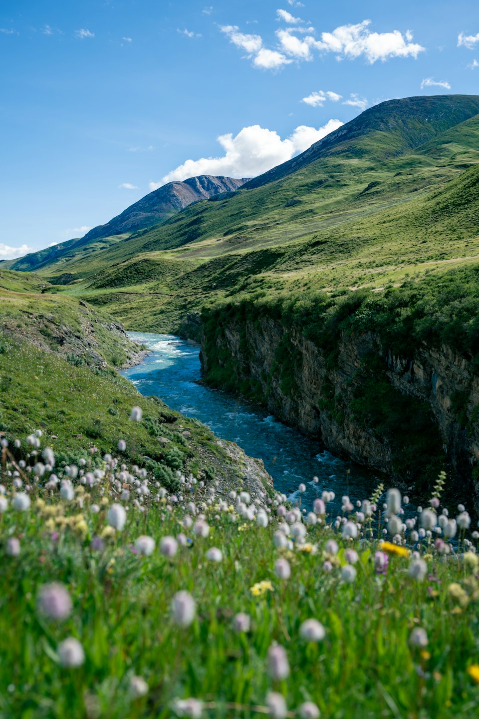 Turquoise river flowing through a rocky canyon between rolling hills.